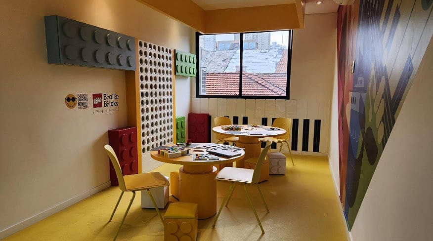 Foto mostra a sala do projeto LEGO Braille Bricks. Ao centro, duas mesas com os kit do LEGO Brille Bricks,